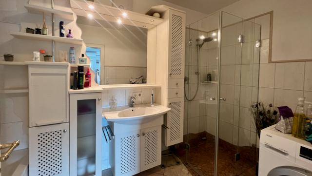Modernes Badezimmer mit Duschkabine, Waschtisch und Spiegelschrank, hell gefliest.