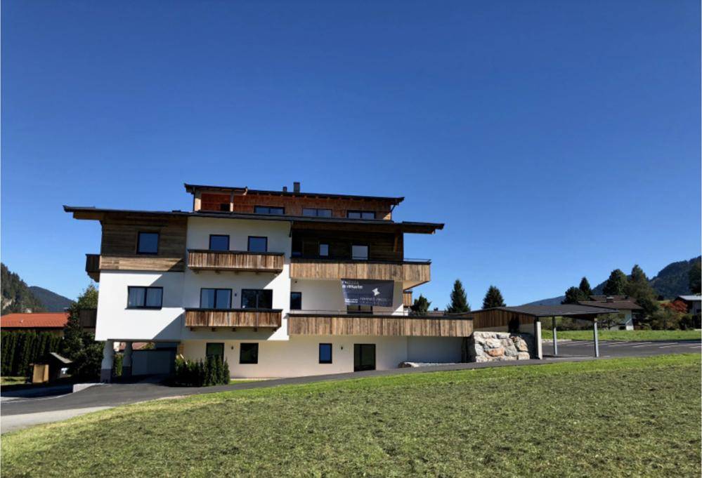 Modernes Wohngebäude mit Holzverkleidung und Balkonen, umgeben von grünen Hügeln und Bergen.