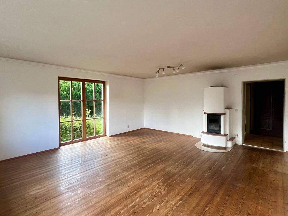 Helles Wohnzimmer mit Holzboden, großem Fenster und einem gemütlichen Kaminofen.