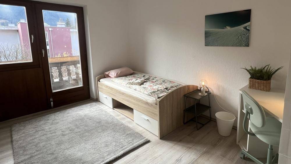 Gemütliches Schlafzimmer mit Einzelbett, Schreibtisch und Zugang zu einem kleinen Balkon mit Bergblick.