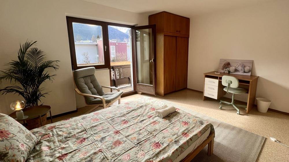 Gemütliches Schlafzimmer mit Schreibtisch, Kleiderschrank und Balkonzugang mit Bergsicht.
