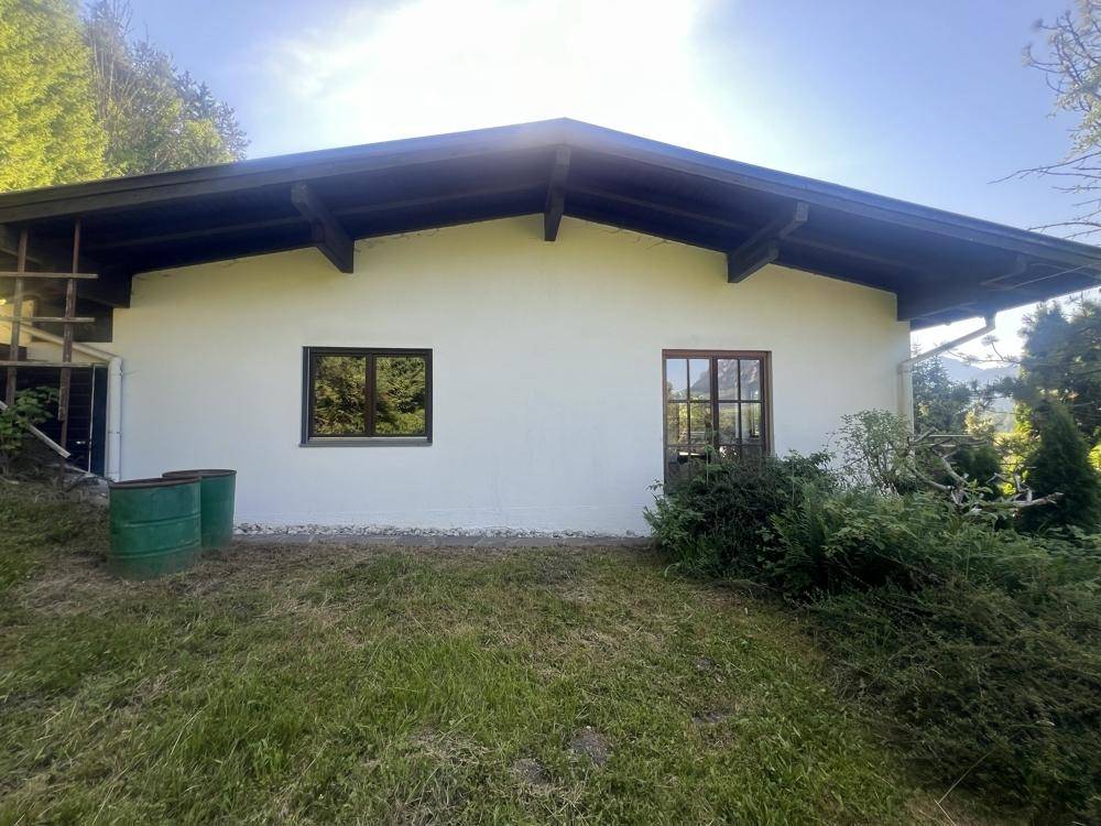 Seitenansicht des Hauses mit weißer Fassade, Fenstern und einem grünen Rasen im Vordergrund.
