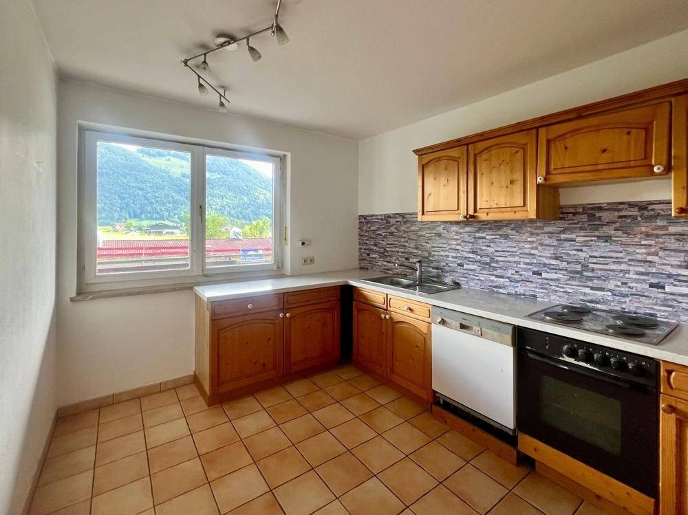 Traditionelle Küche mit Holzschränken, Fliesenboden und einem Fenster mit Bergblick.