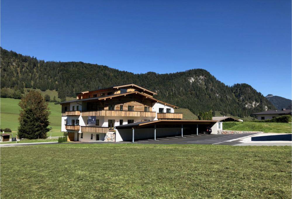 Neubau im alpinen Stil mit Holzfassade und Carport, eingebettet in eine grüne Berglandschaft.