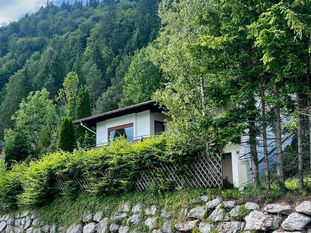 Das Haus fügt sich harmonisch in die bewaldete Hanglage ein, umgeben von viel Grün.