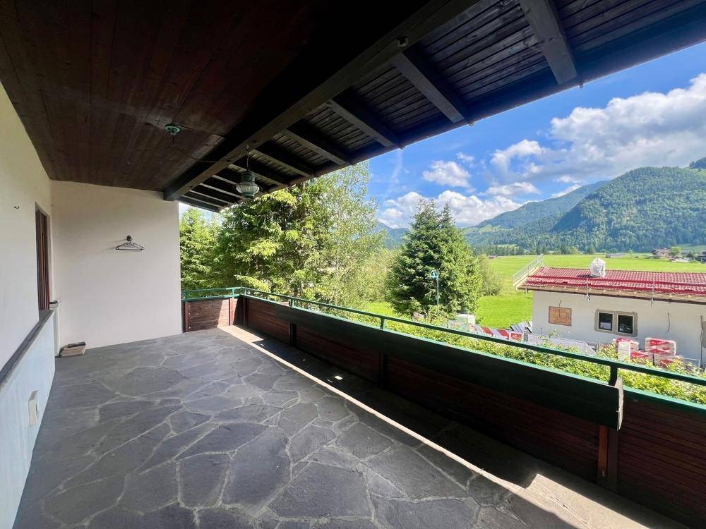 Geräumiger Balkon mit Steinplattenboden und weitem Blick auf die grüne Berglandschaft.