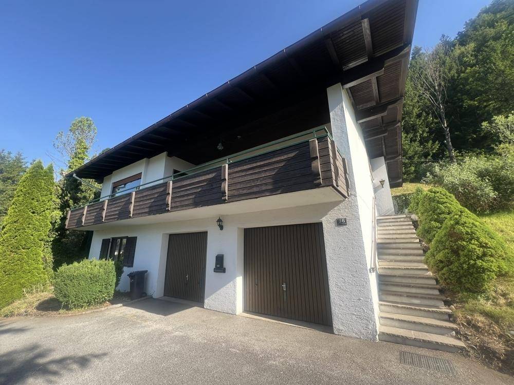 Vorderansicht des Hauses mit zwei Garagen und einer Außentreppe, umgeben von Grün.