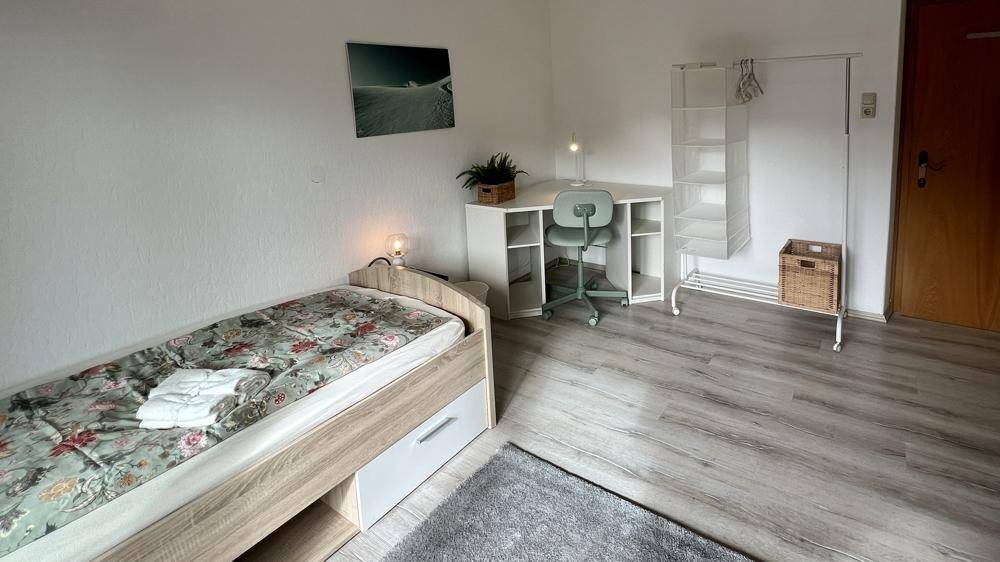 Helles Schlafzimmer mit Einzelbett, Schreibtisch und praktischem Kleiderständer.