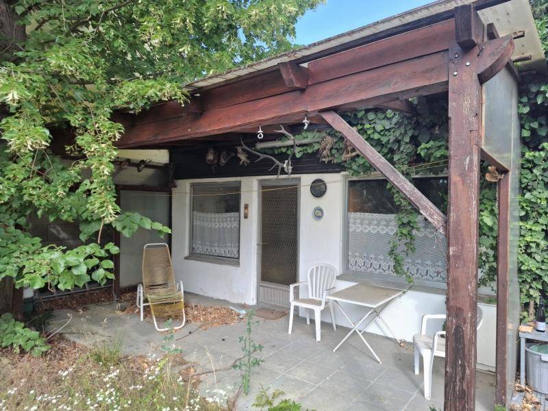 Kleine überdachte Terrasse mit einfachen Gartenmöbeln und viel Grün, ideal für entspannte Stunden im Freien.