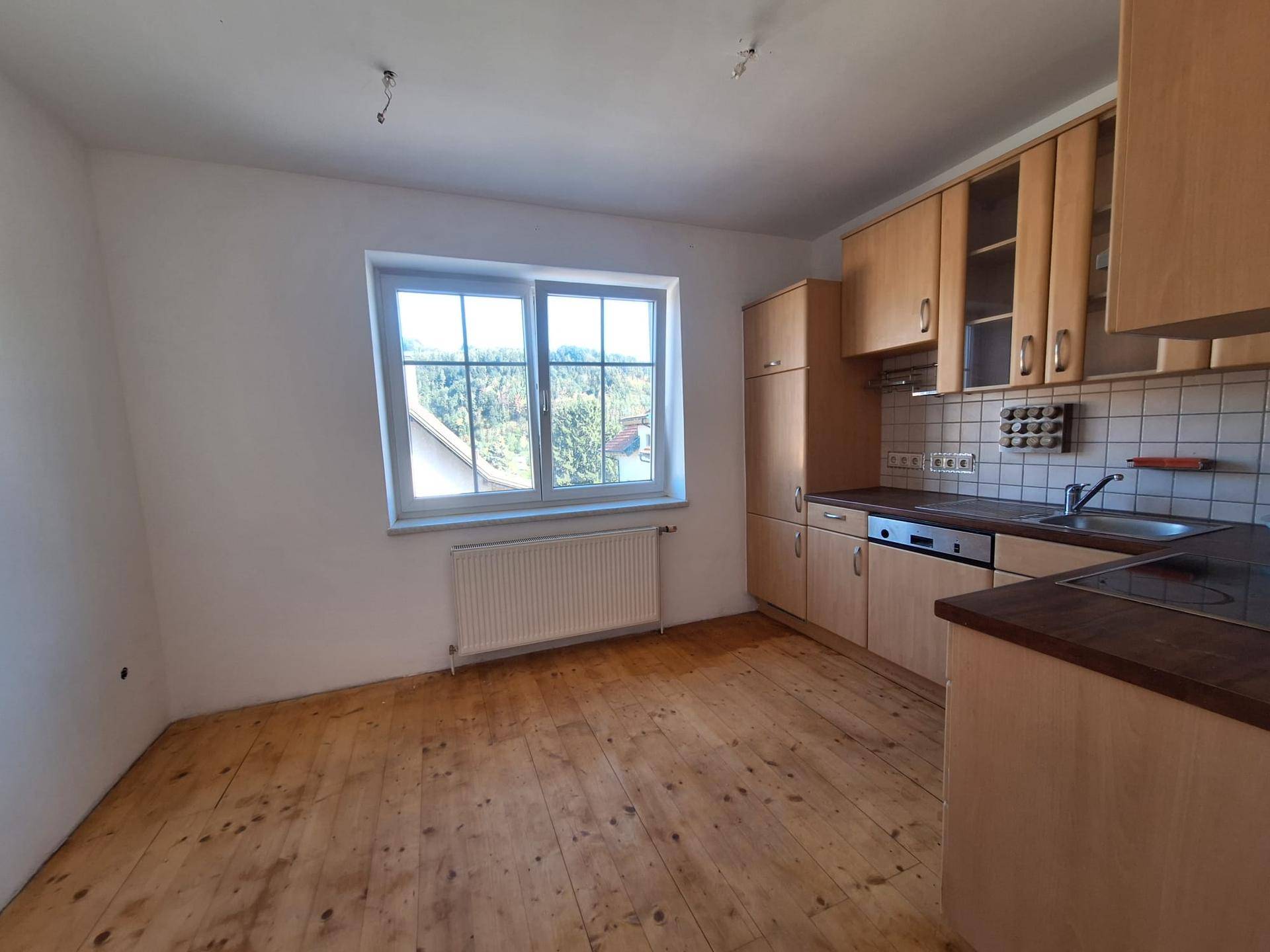 Helle Küche mit Holzschränken, Fliesenrückwand und Blick ins Grüne durch das Fenster.