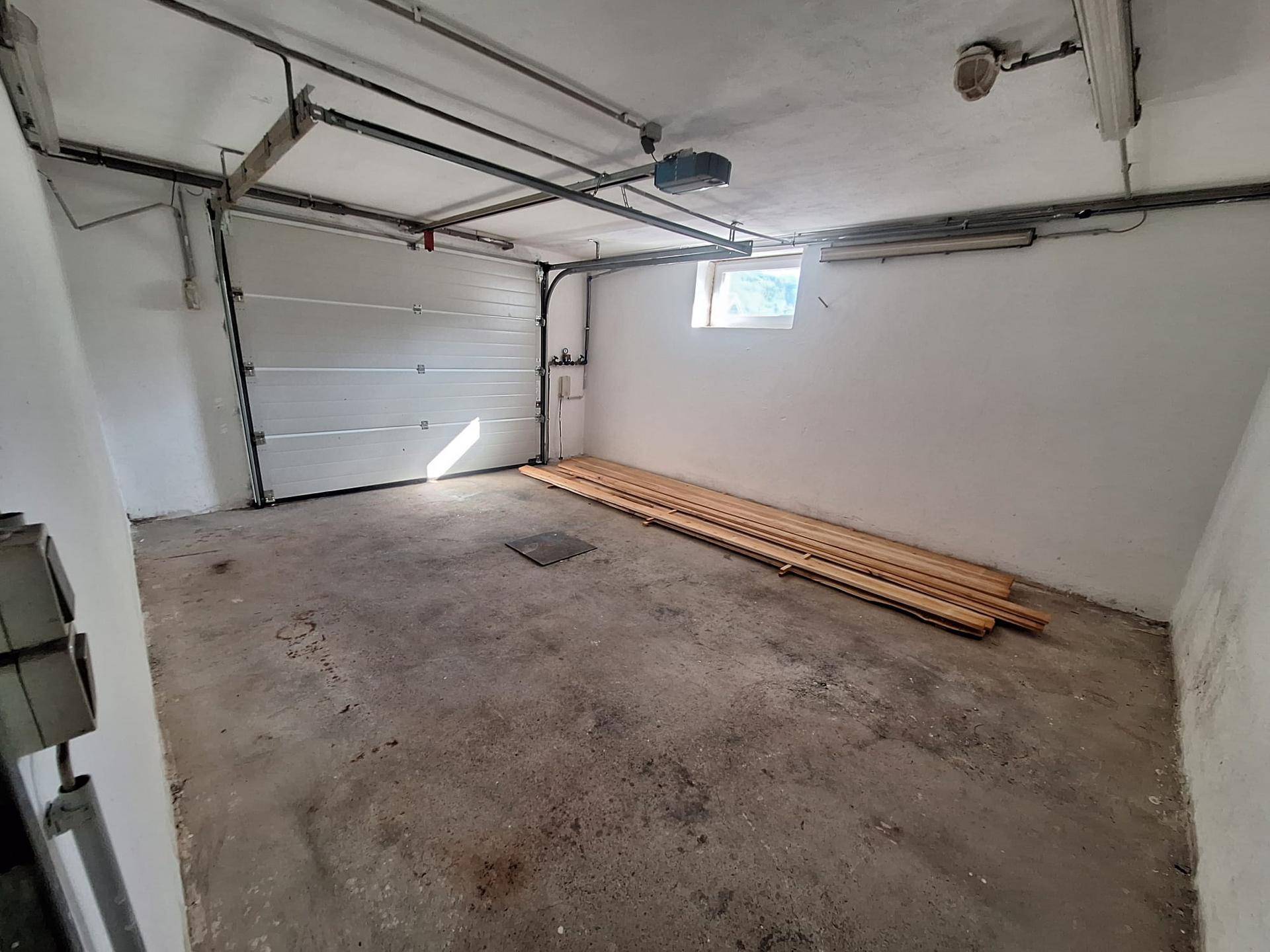 Geräumige Garage mit Betonboden, Rolltor und einem kleinen Fenster für Tageslicht.