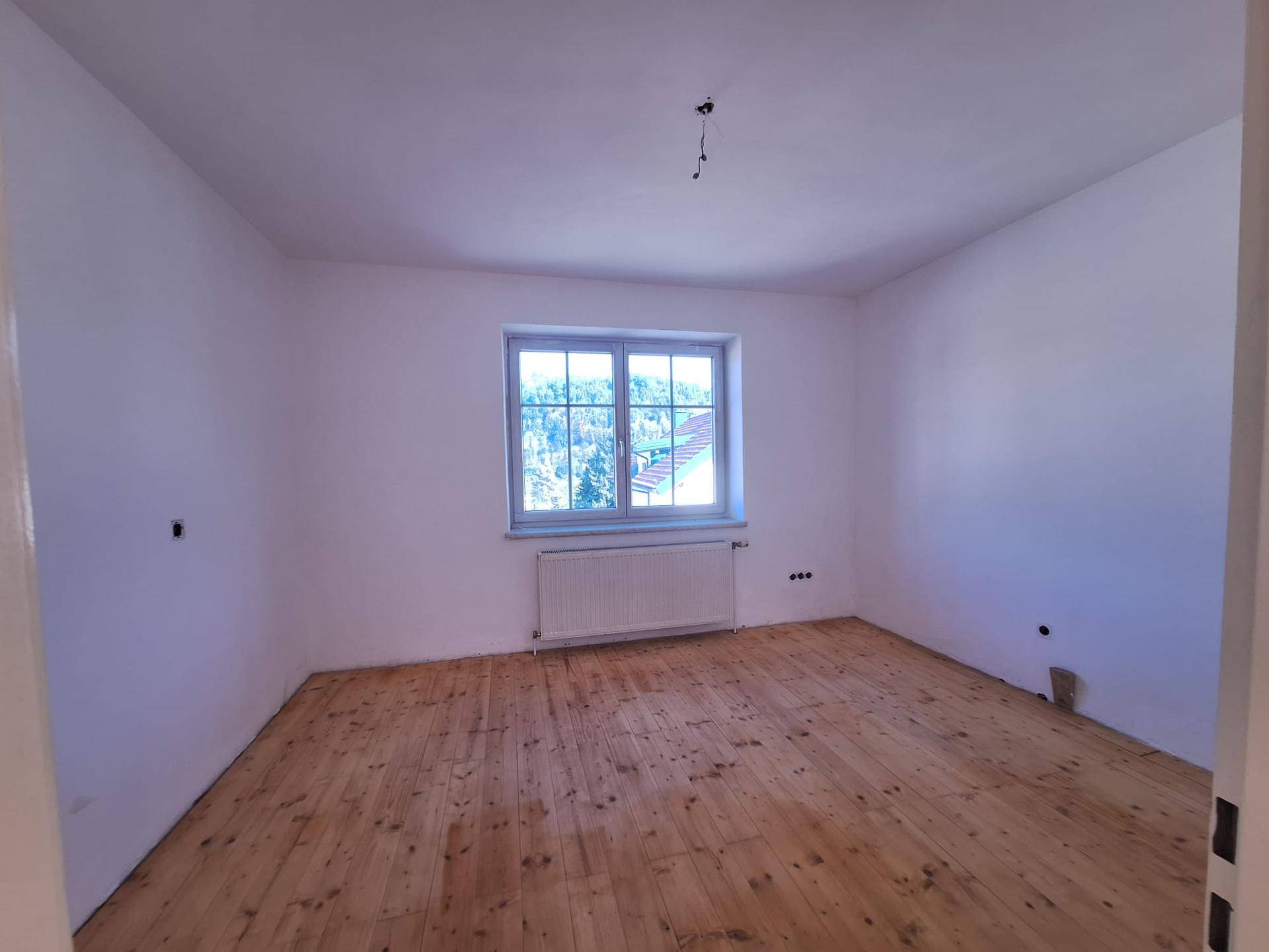 Geräumiges Schlafzimmer mit Holzdielenboden und einem großen Fenster, das viel Licht hereinlässt.