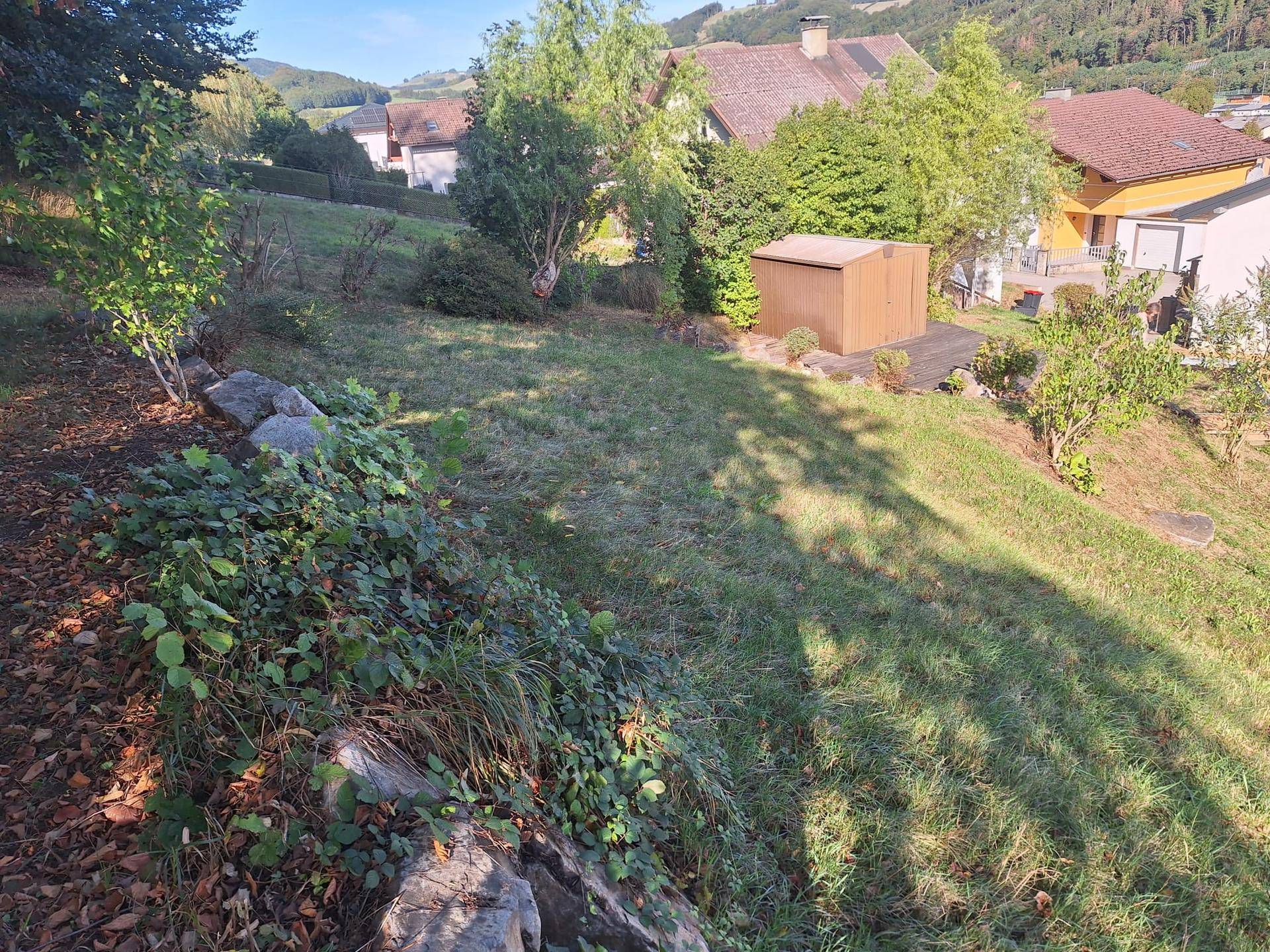 Abfallender Gartenbereich mit natürlicher Bepflanzung und Blick auf die umliegende Landschaft.