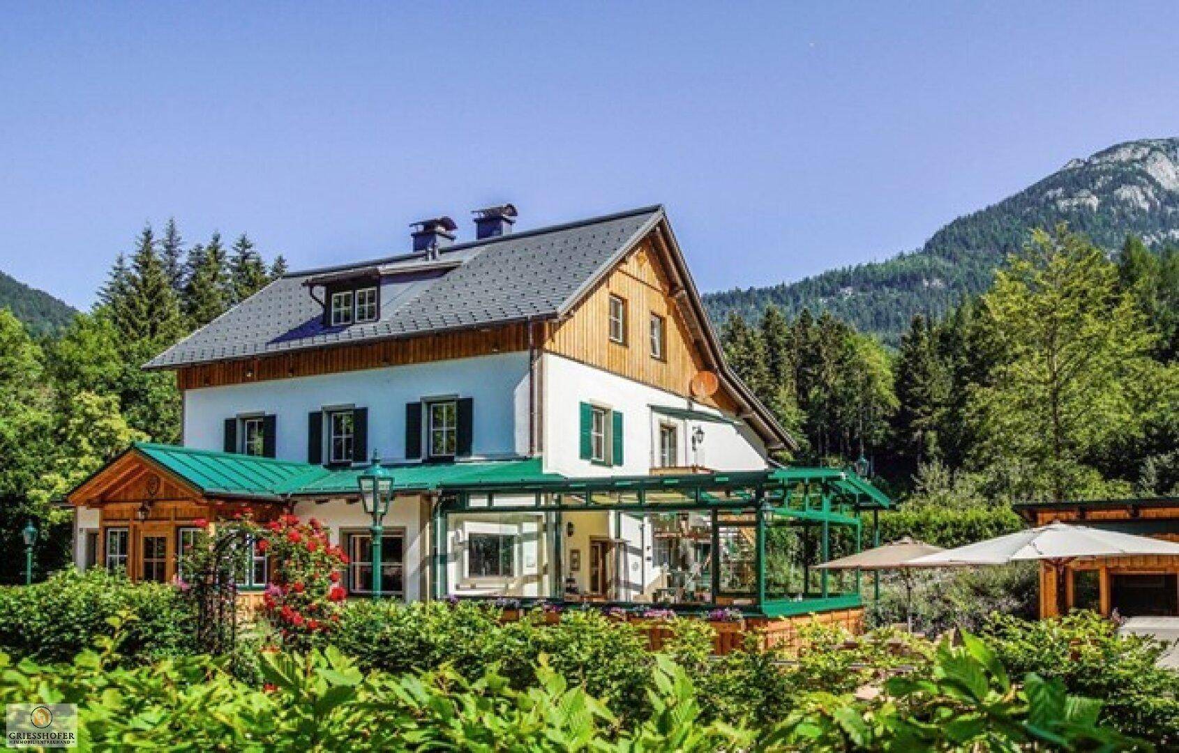 Großes Landhaus mit grüner Veranda und weitläufigem Garten in alpiner Umgebung.