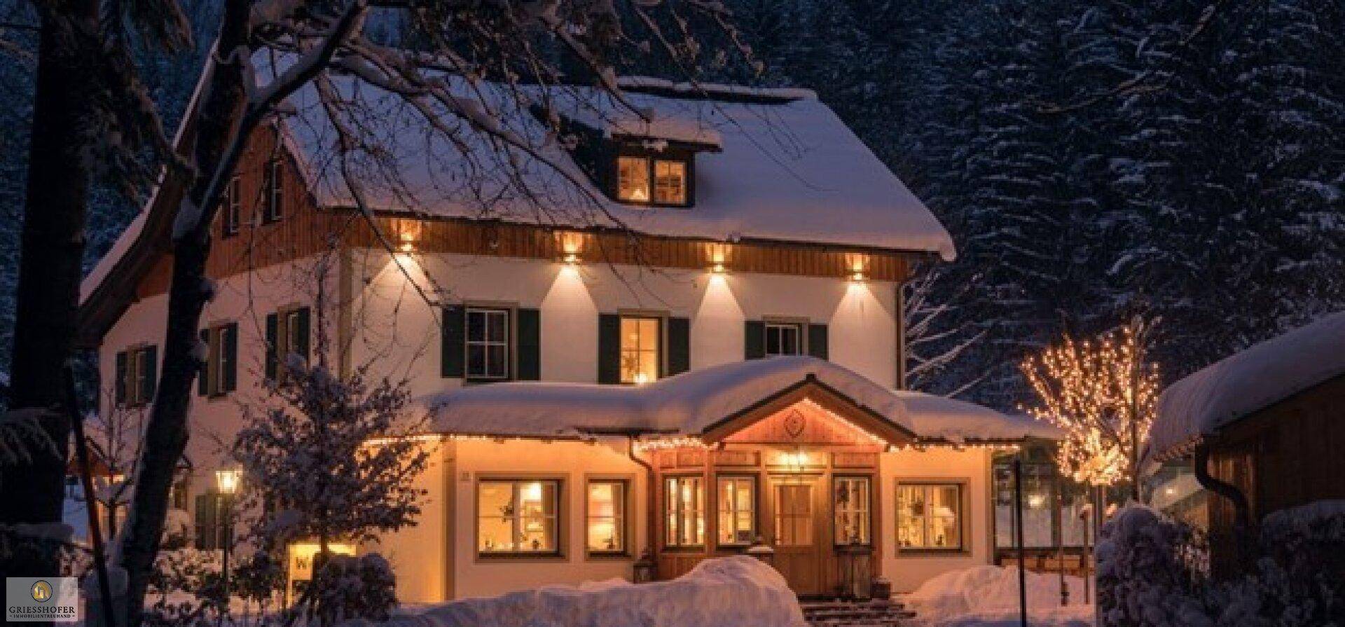 Winterliche Ansicht eines traditionellen Hauses mit beleuchteter Fassade und Schnee.