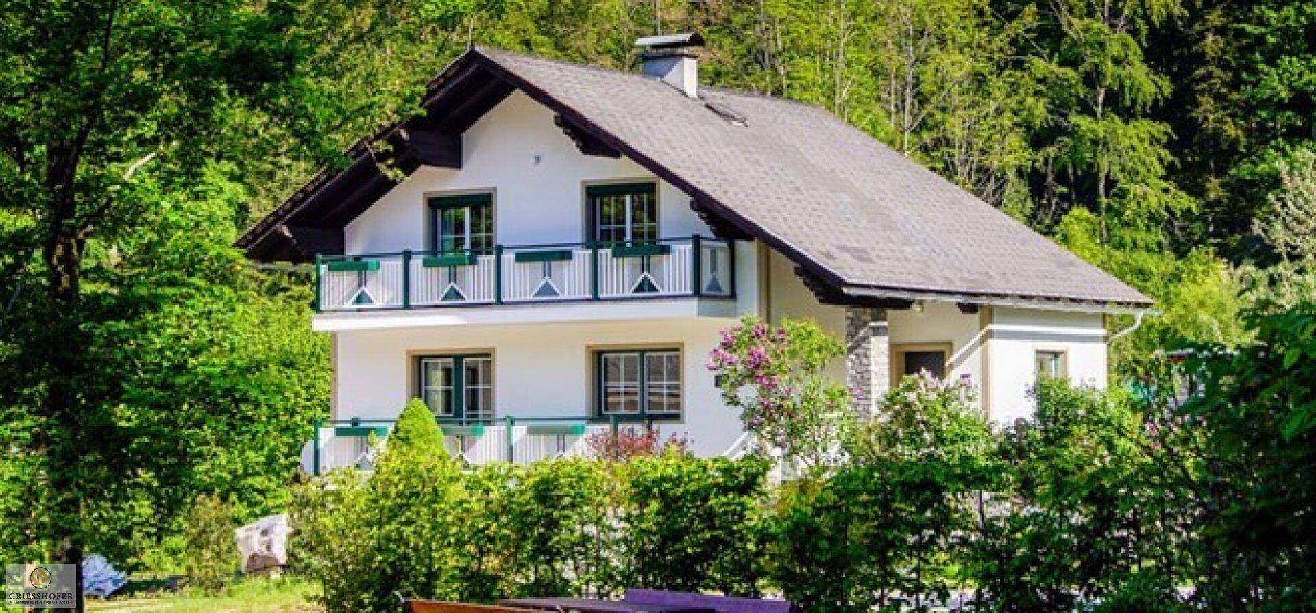 Charmantes Haus mit Balkonen und grünen Fensterläden, umgeben von Bäumen.