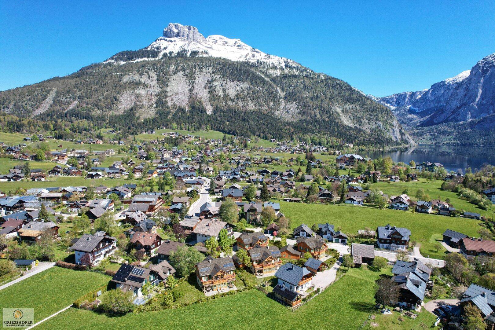 Panoramablick aus der Vogelperspektive auf ein malerisches Dorf am Seeufer, umgeben von majestätischen Bergen.
