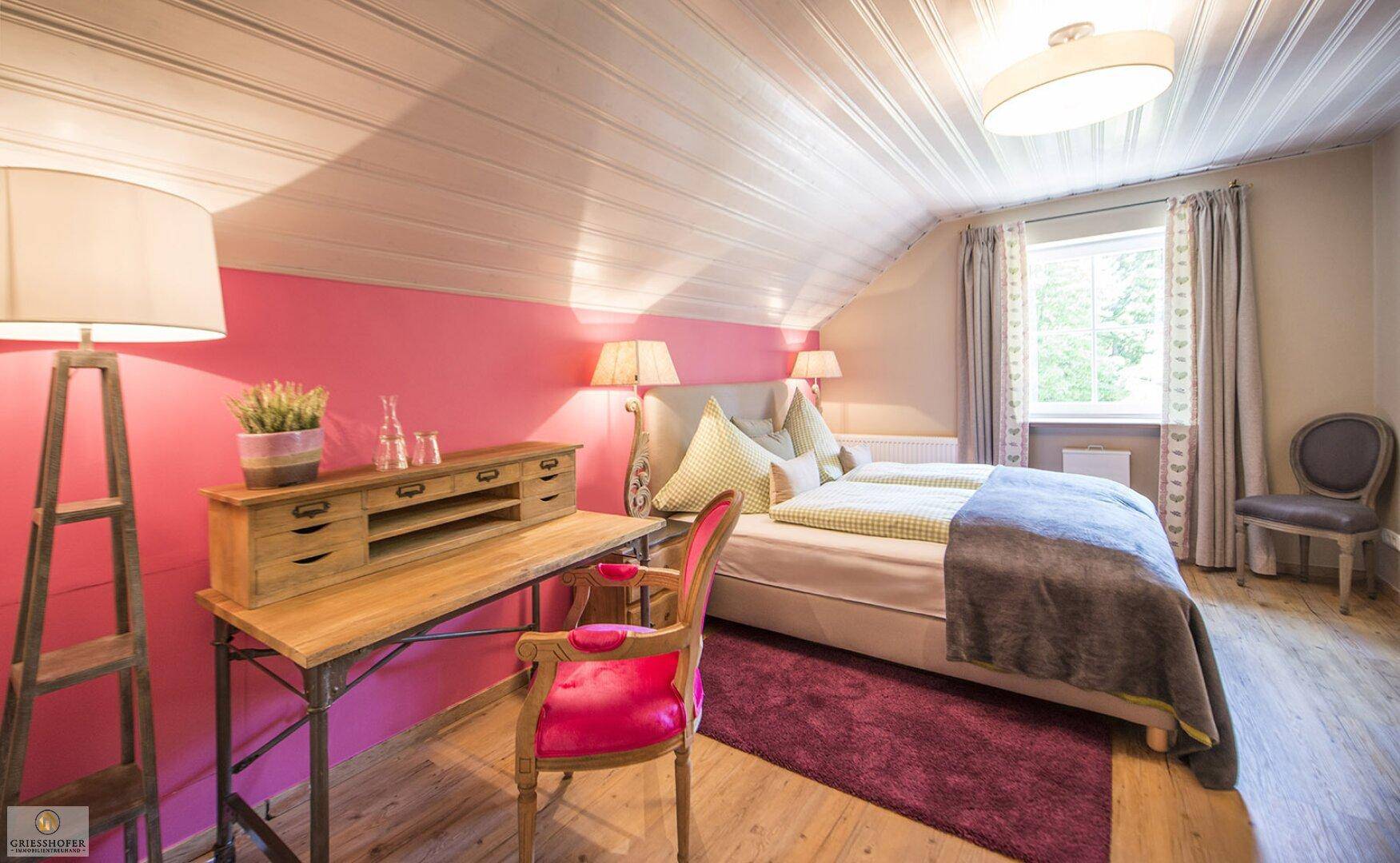 Schlafzimmer im Dachgeschoss mit pinker Wand, Holzboden und Schreibtisch.