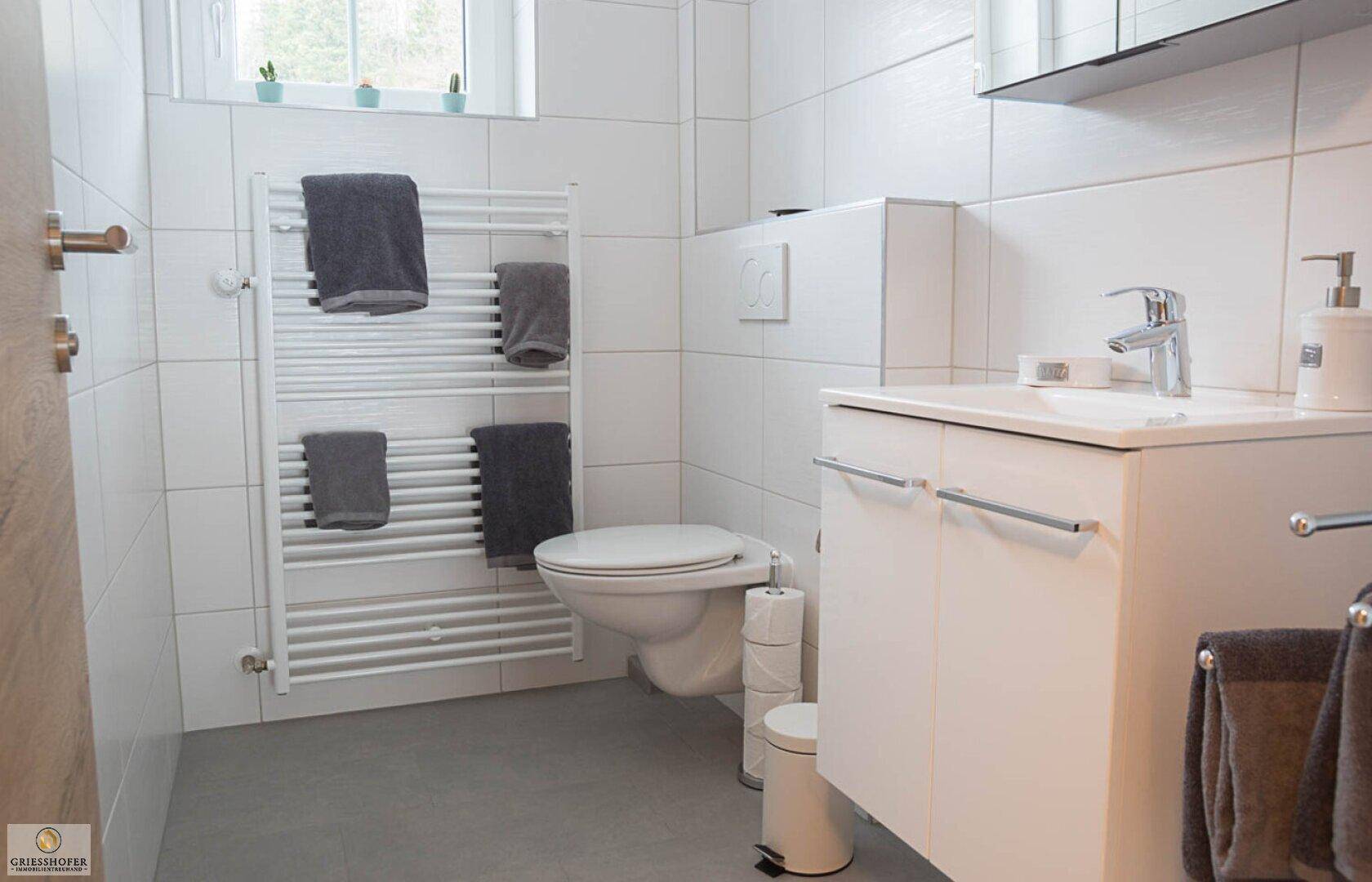 Modernes Badezimmer mit weißen Fliesen, wandhängendem WC und Handtuchheizkörper.