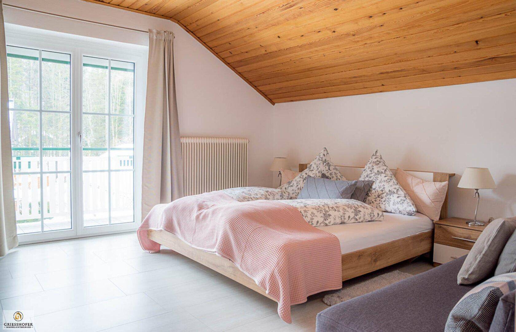 Helles Schlafzimmer mit Holzdachschräge, Balkonzugang und Doppelbett.