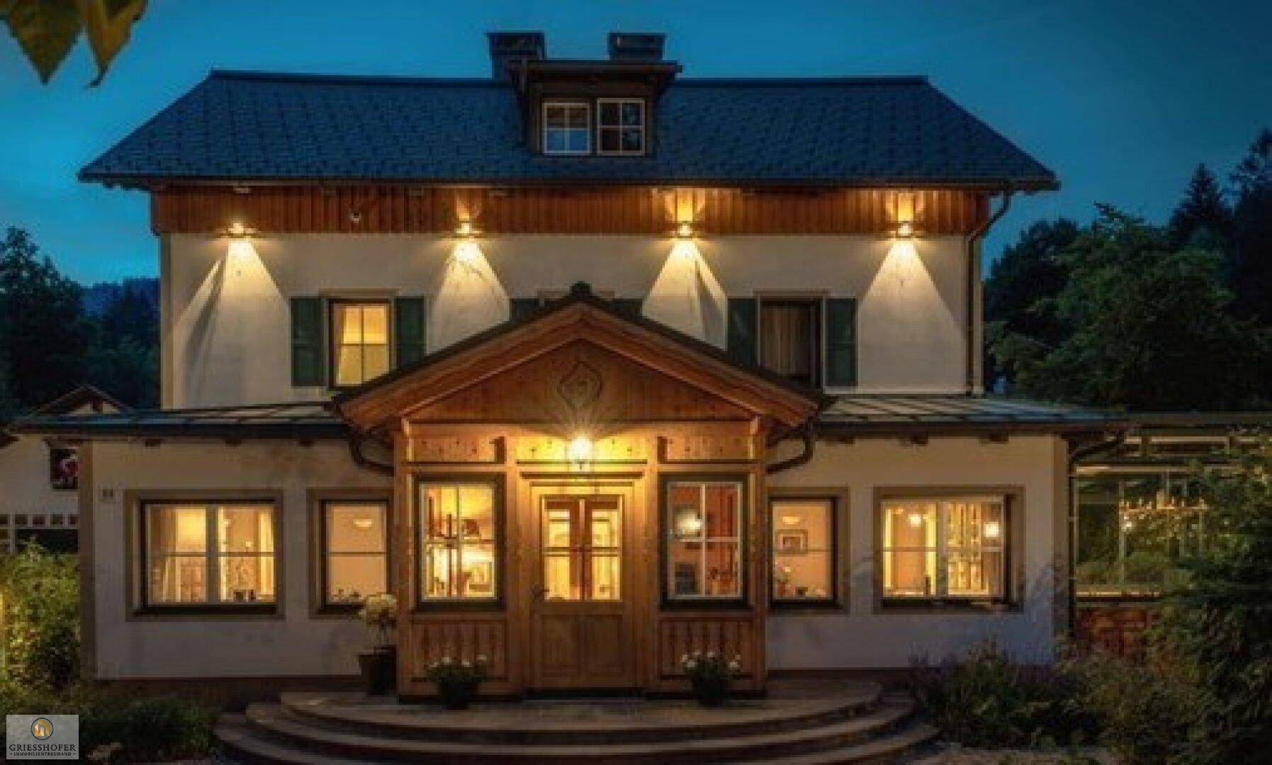 Traditionelles Haus mit beleuchteter Fassade und Holzelementen bei Dämmerung.