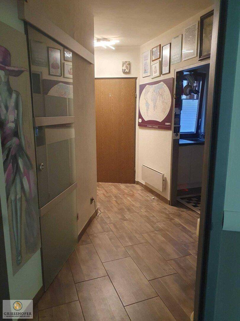 Heller Flur mit Fliesenboden in Holzoptik und gerahmten Bildern an den Wänden.