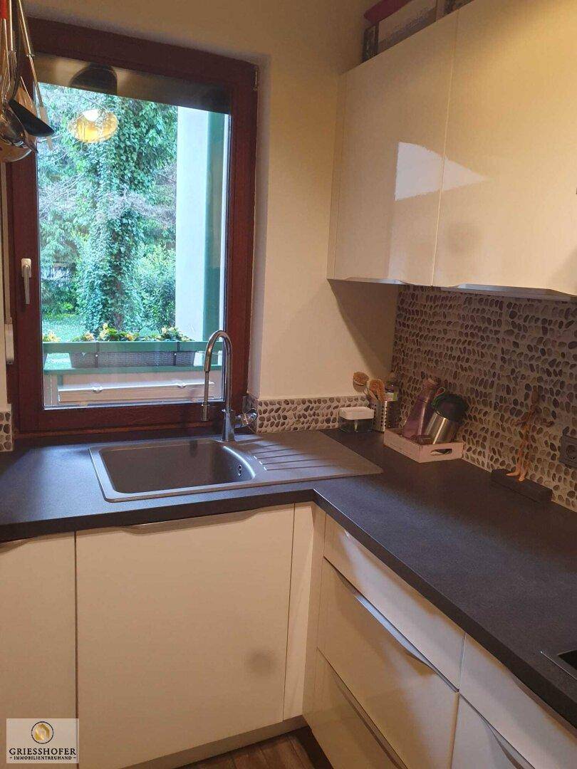 Moderne Küche mit weißer Spüle, dunkler Arbeitsplatte und Fenster mit Blick ins Grüne.