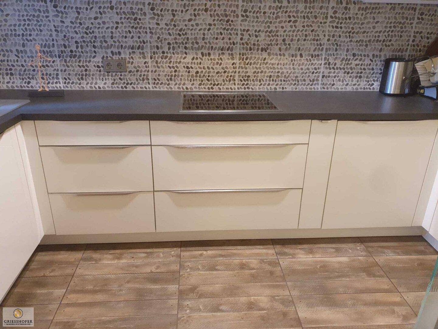 Küchenzeile mit Induktionskochfeld, weißen Schränken und dekorativem Fliesen-Spritzschutz.