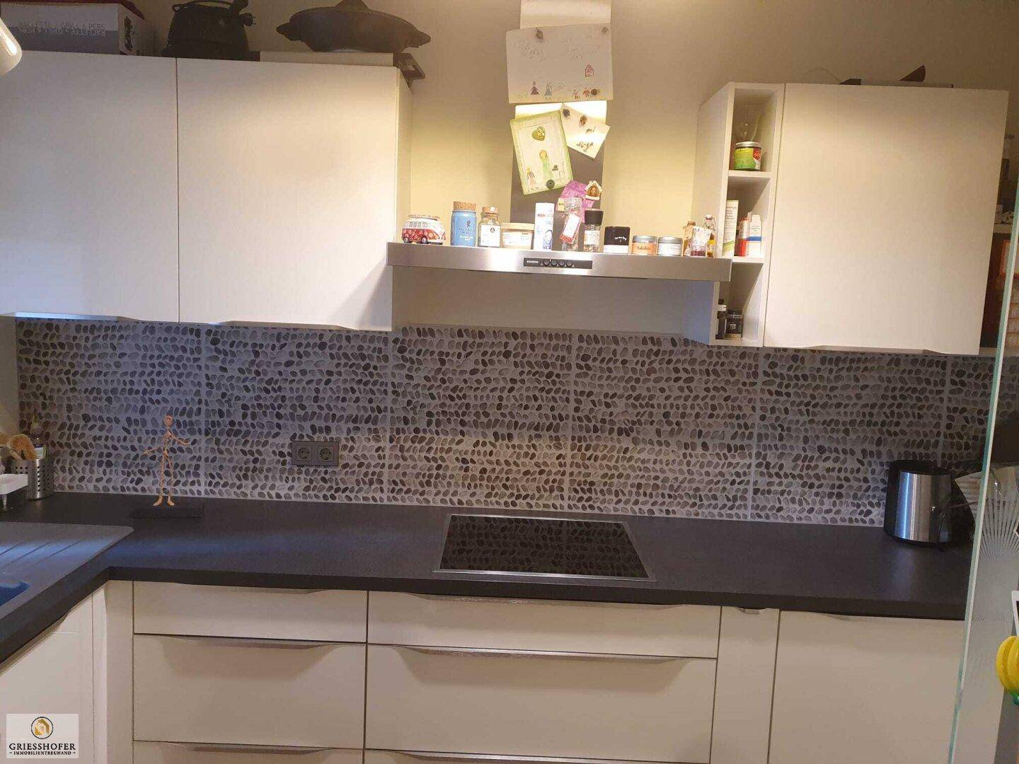 Moderne Küche mit Dunstabzugshaube, weißen Schränken und Steinmosaik-Fliesen an der Wand.