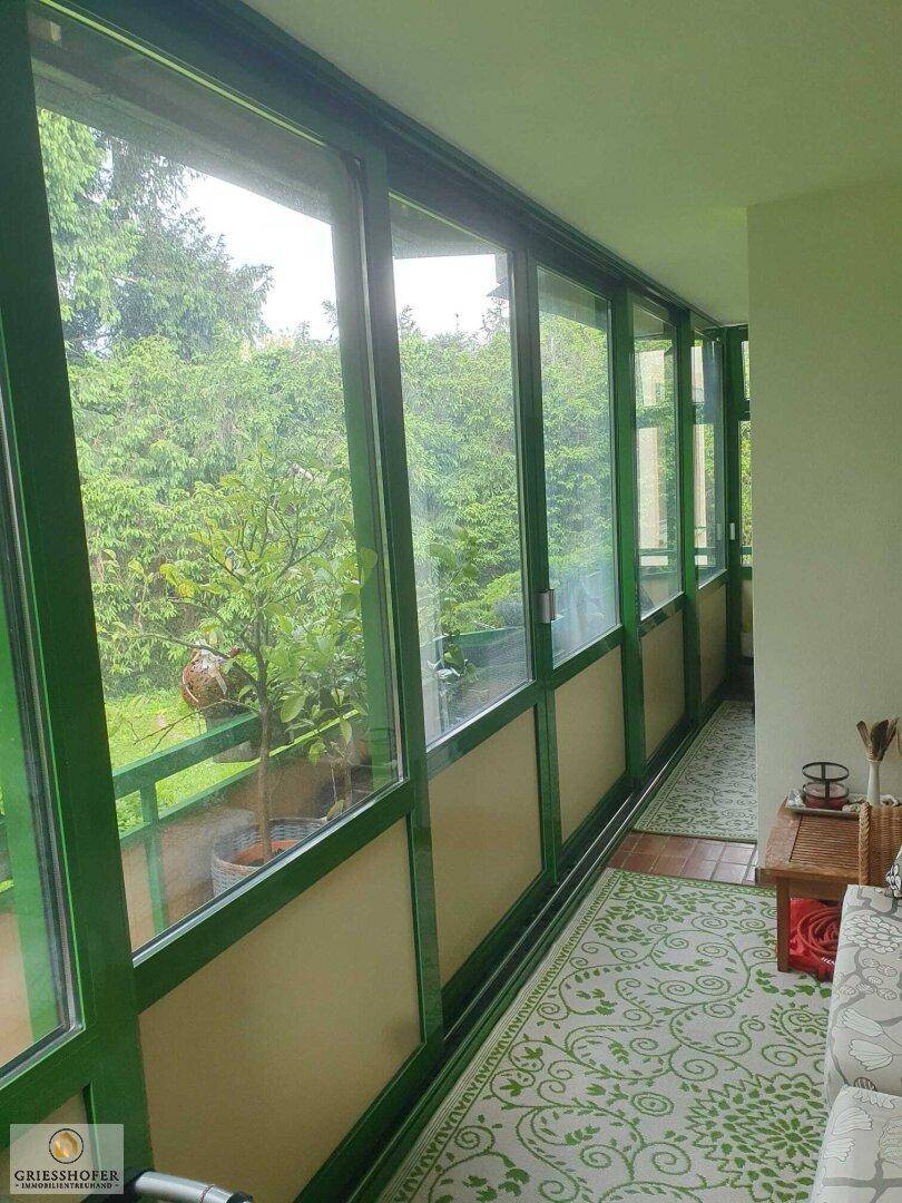 Lange verglaste Loggia mit grünen Fensterrahmen und weitem Blick ins Grüne.