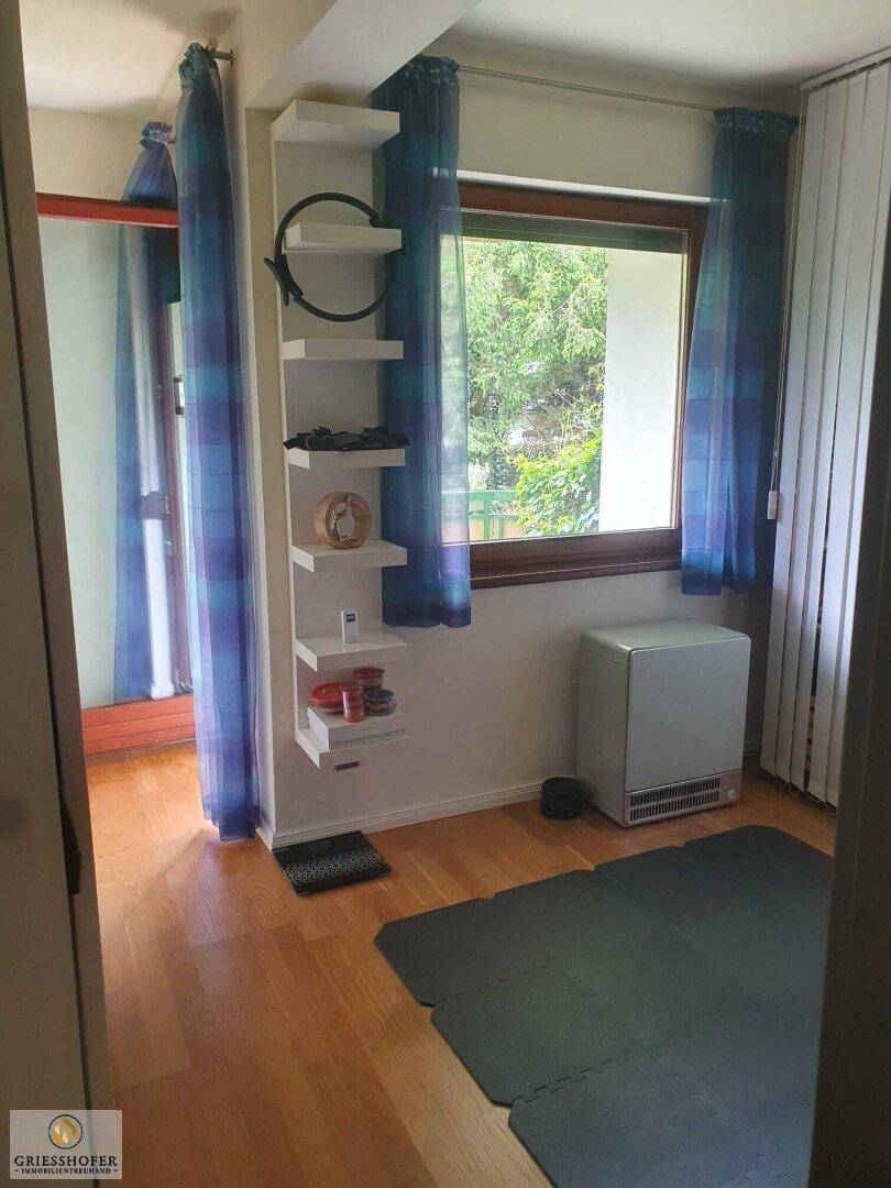 Vielseitiger Raum mit Holzboden, Fenster und blauen Vorhängen, ideal als Schlaf- oder Arbeitszimmer.