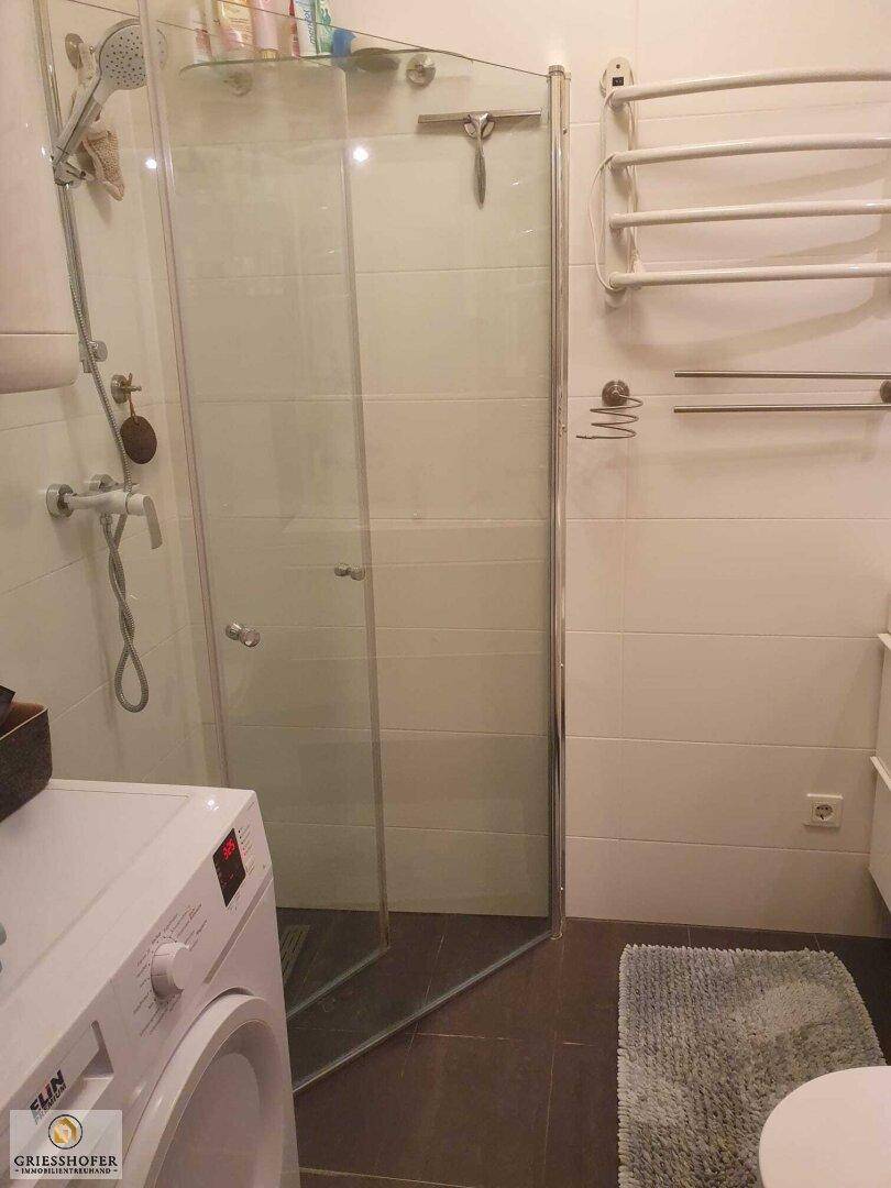 Modernes Badezimmer mit Duschkabine, Waschmaschine und beheiztem Handtuchhalter.