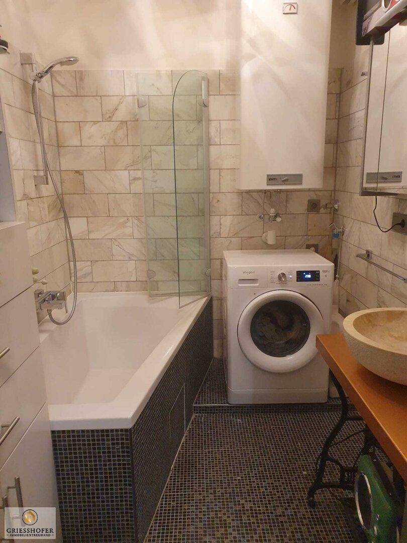 Badezimmer mit Badewanne, Waschmaschine und stilvollem Aufsatzwaschbecken.