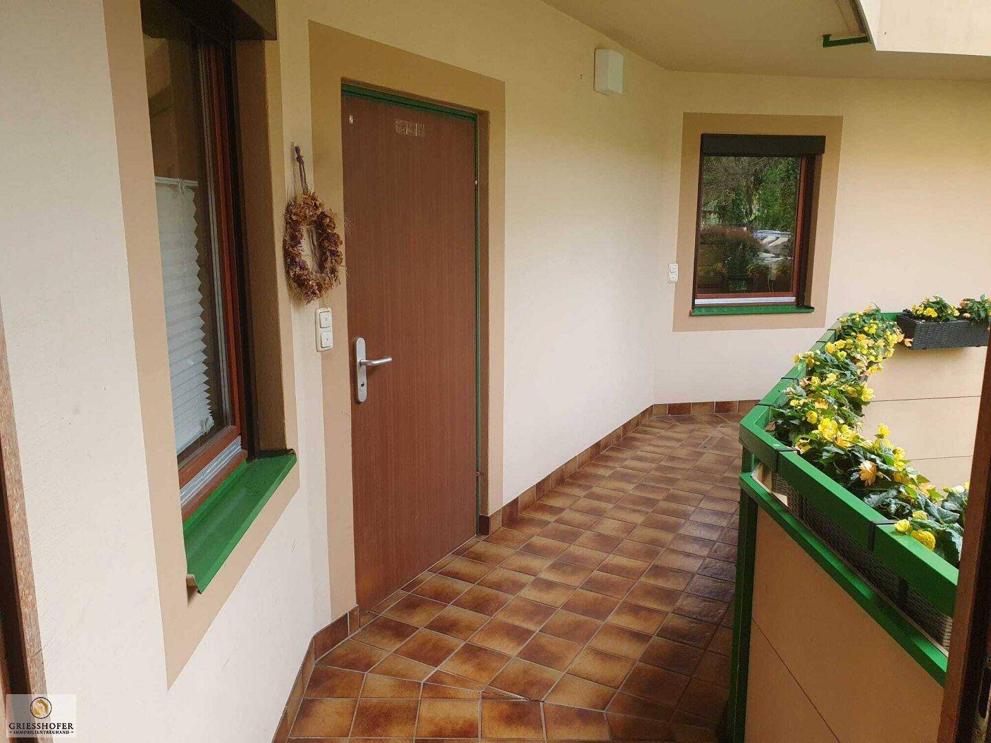 Überdachter Eingangsbereich mit Fliesenboden und Blumenkästen am Geländer.