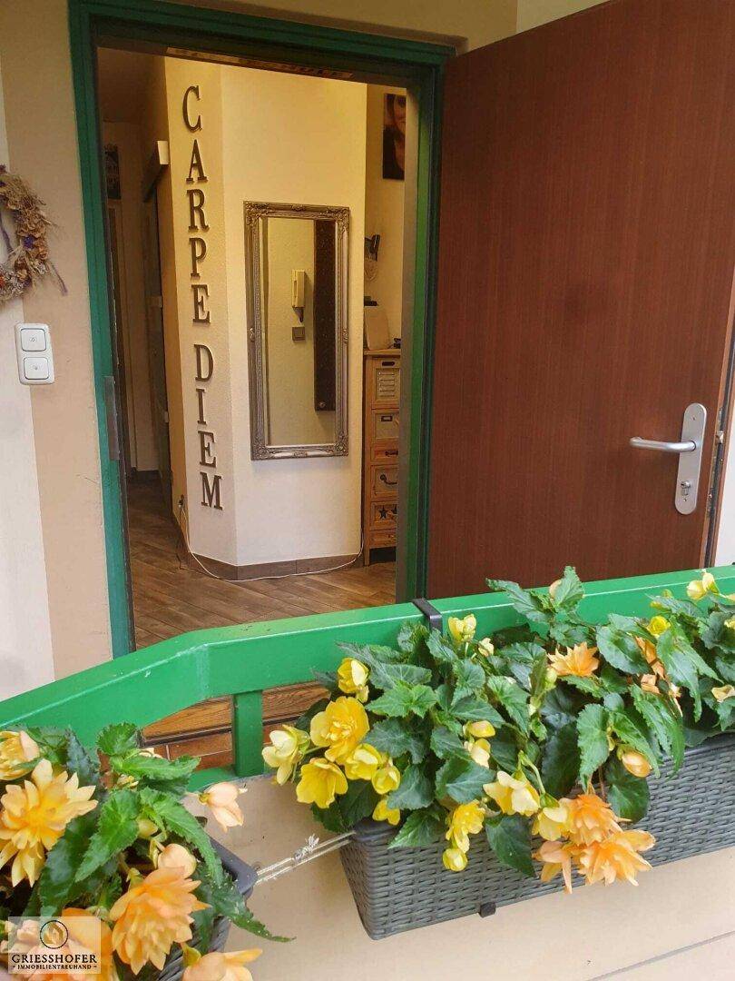 Eingangstür vom Balkon aus gesehen, umgeben von Blumen und mit Blick in den Flur.