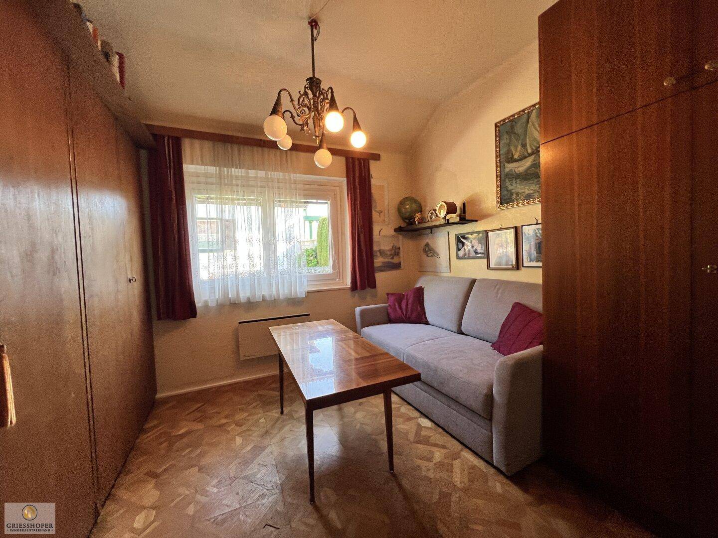 Kleines Zimmer mit Sofa, Holzeinbauschränken und gemustertem Parkettboden.