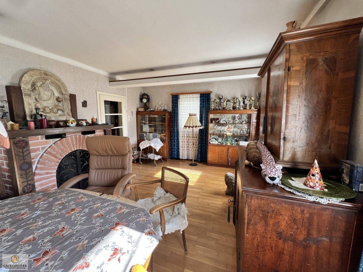 Traditioneller Wohnbereich mit Kamin, Holzboden und antiken Vitrinen.