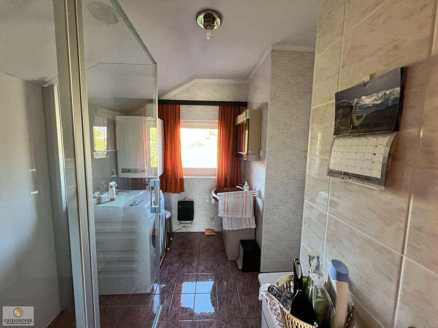 Helles Badezimmer mit Dusche, Waschbecken und Waschmaschine, gefliest.