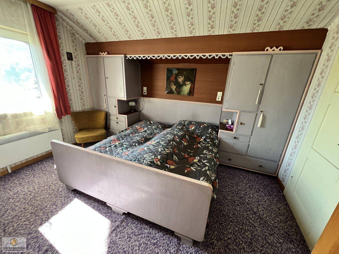Schlafzimmer mit Doppelbett, integrierten Schränken und floraler Tapete.