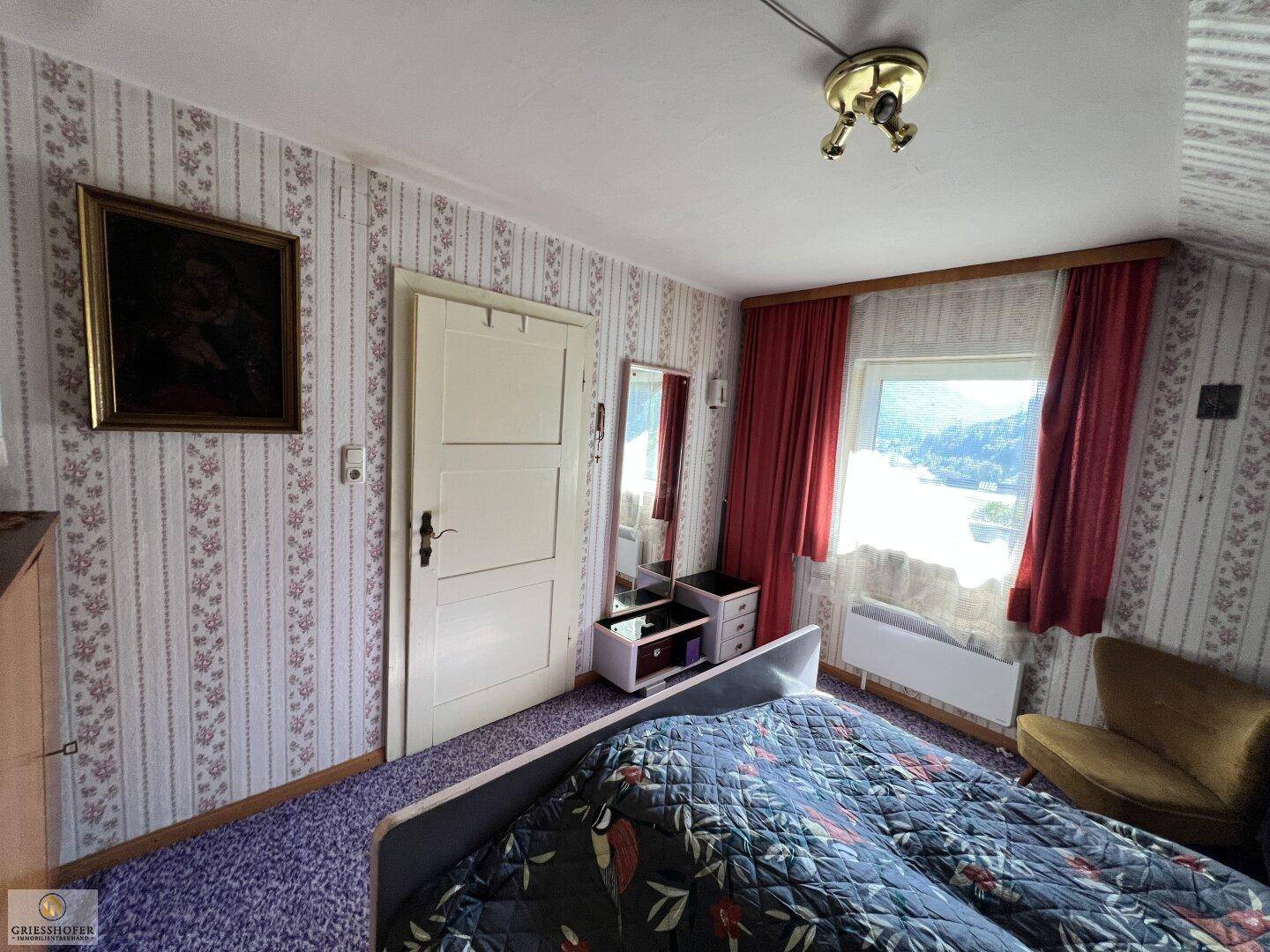 Schlafzimmer mit floraler Tapete, Spiegel und Fenster mit Bergblick.