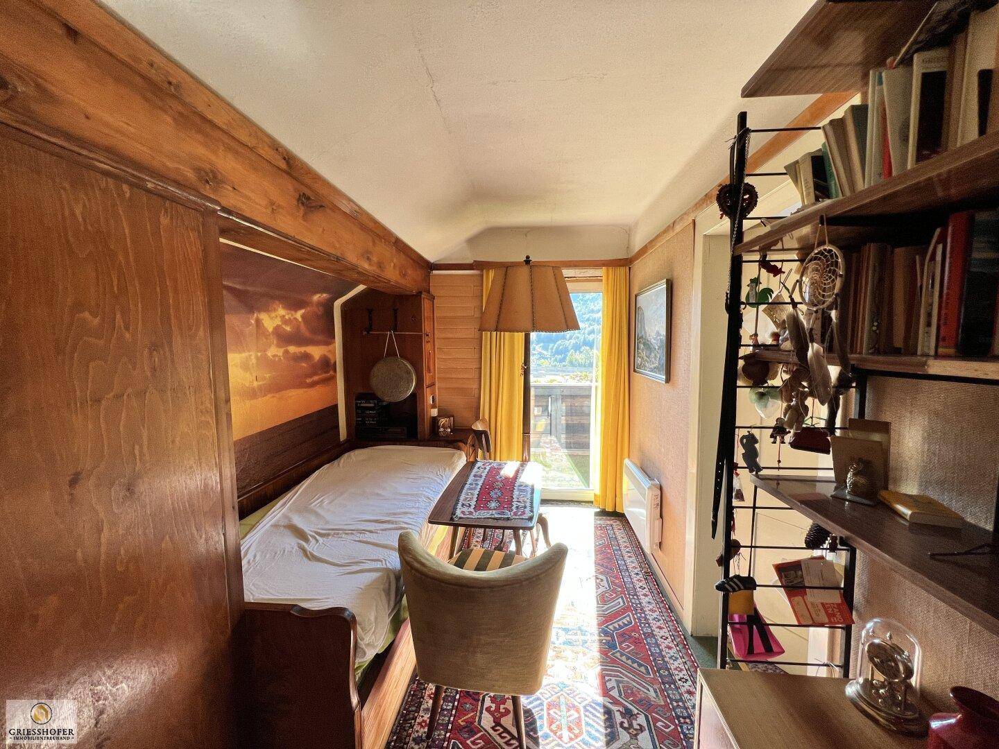 Schlafzimmer mit Holzelementen, Einzelbett und Bücherregal, hell beleuchtet.