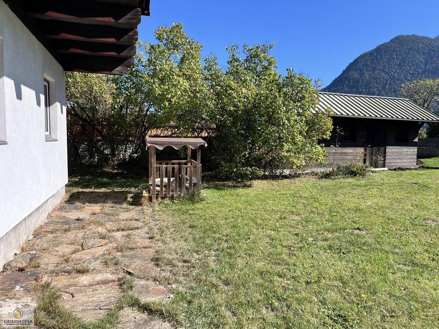 Seitlicher Blick auf das Haus mit einer gepflasterten Fläche und weitläufigem Rasen.