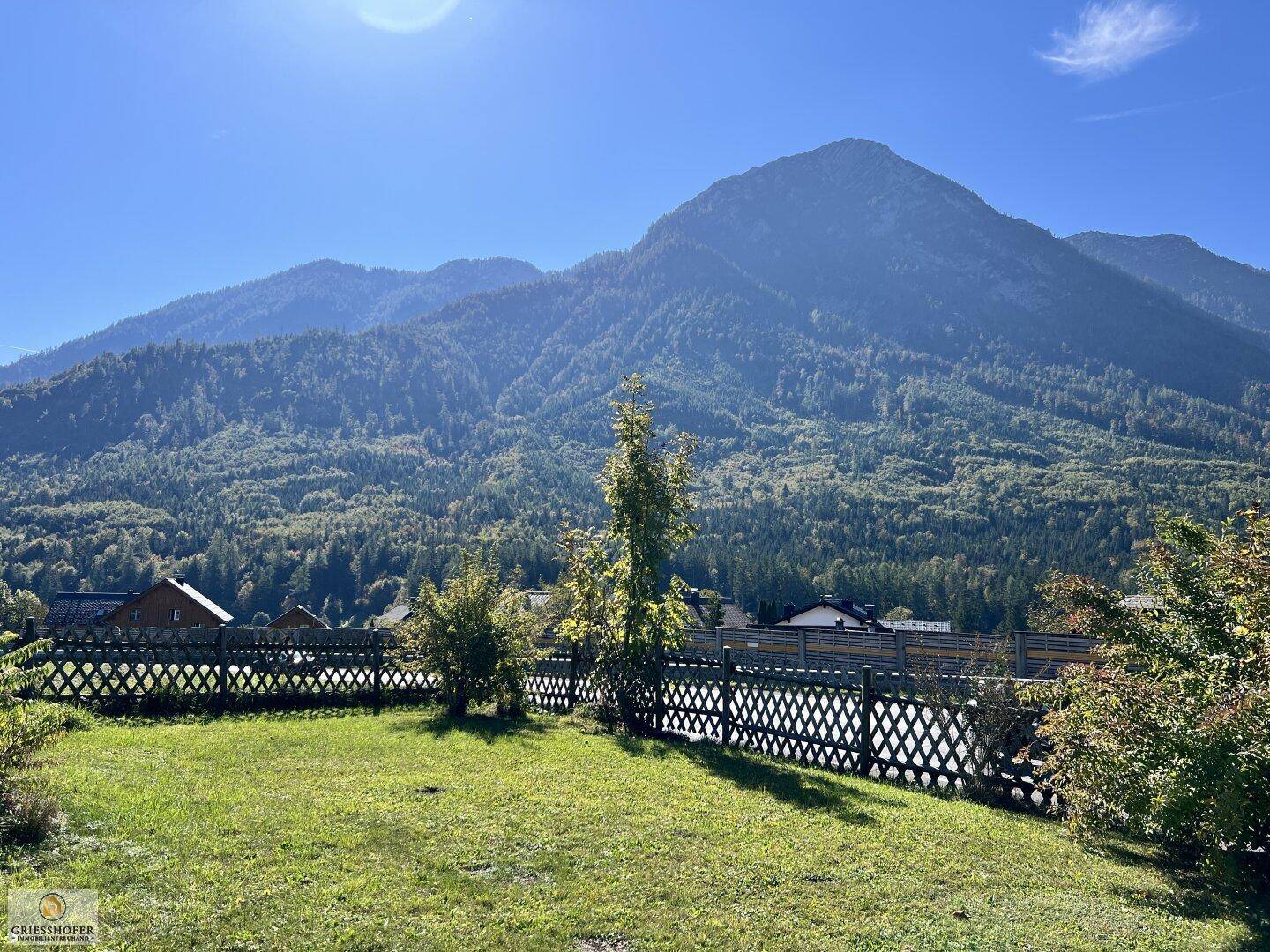 Gepflegter Rasenbereich mit Holzzaun und weitem Blick auf die umliegenden Berge.