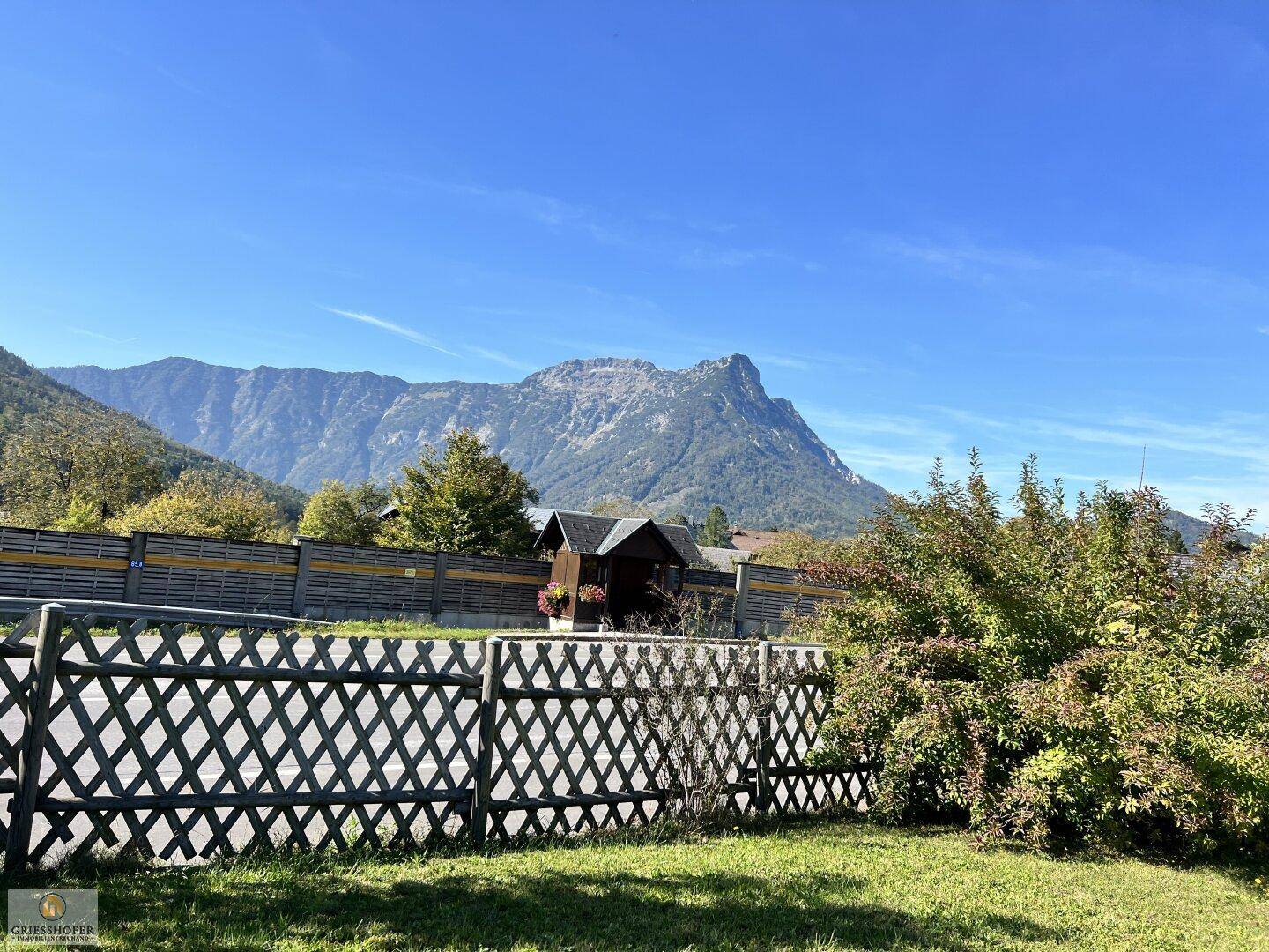 Blick über einen Holzzaun auf die beeindruckende Berglandschaft unter klarem Himmel.