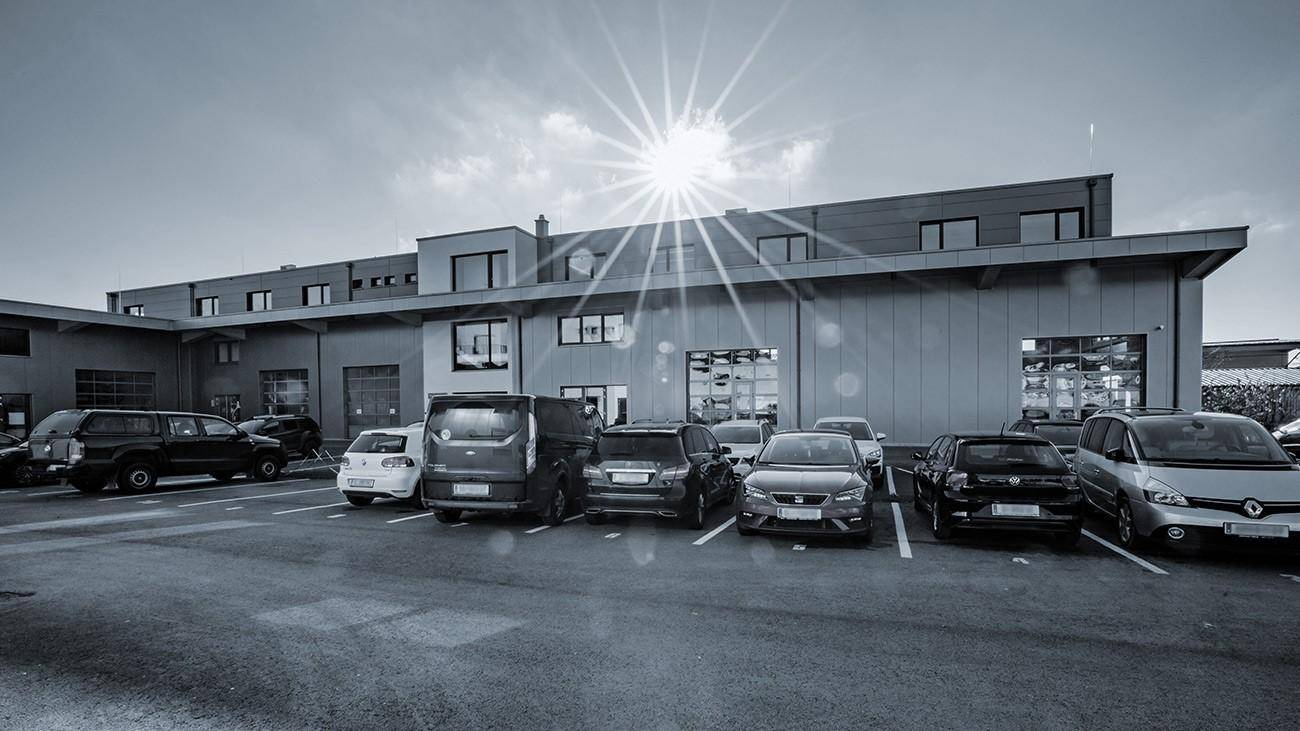 Modernes Geschäftsgebäude mit großem Parkplatz unter strahlendem Himmel und vielen geparkten Autos.