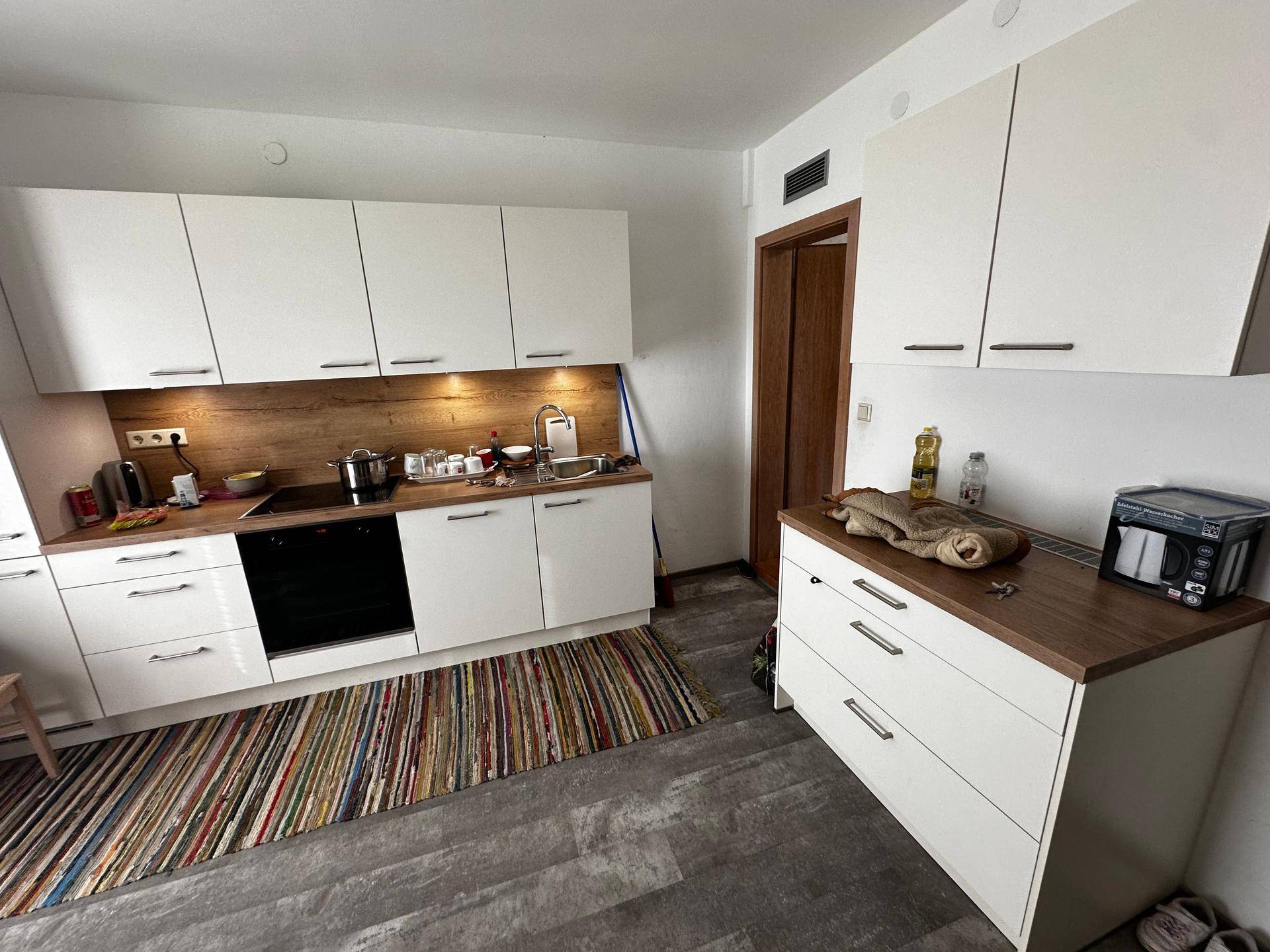 Moderne weiße Küche mit Holz-Arbeitsplatte und integrierten Geräten, dazu ein bunter Teppich.
