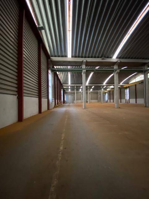 Langer Gang in einer großen Lagerhalle mit Betonpfeilern und gewelltem Metalldach, das Licht hereinlässt.