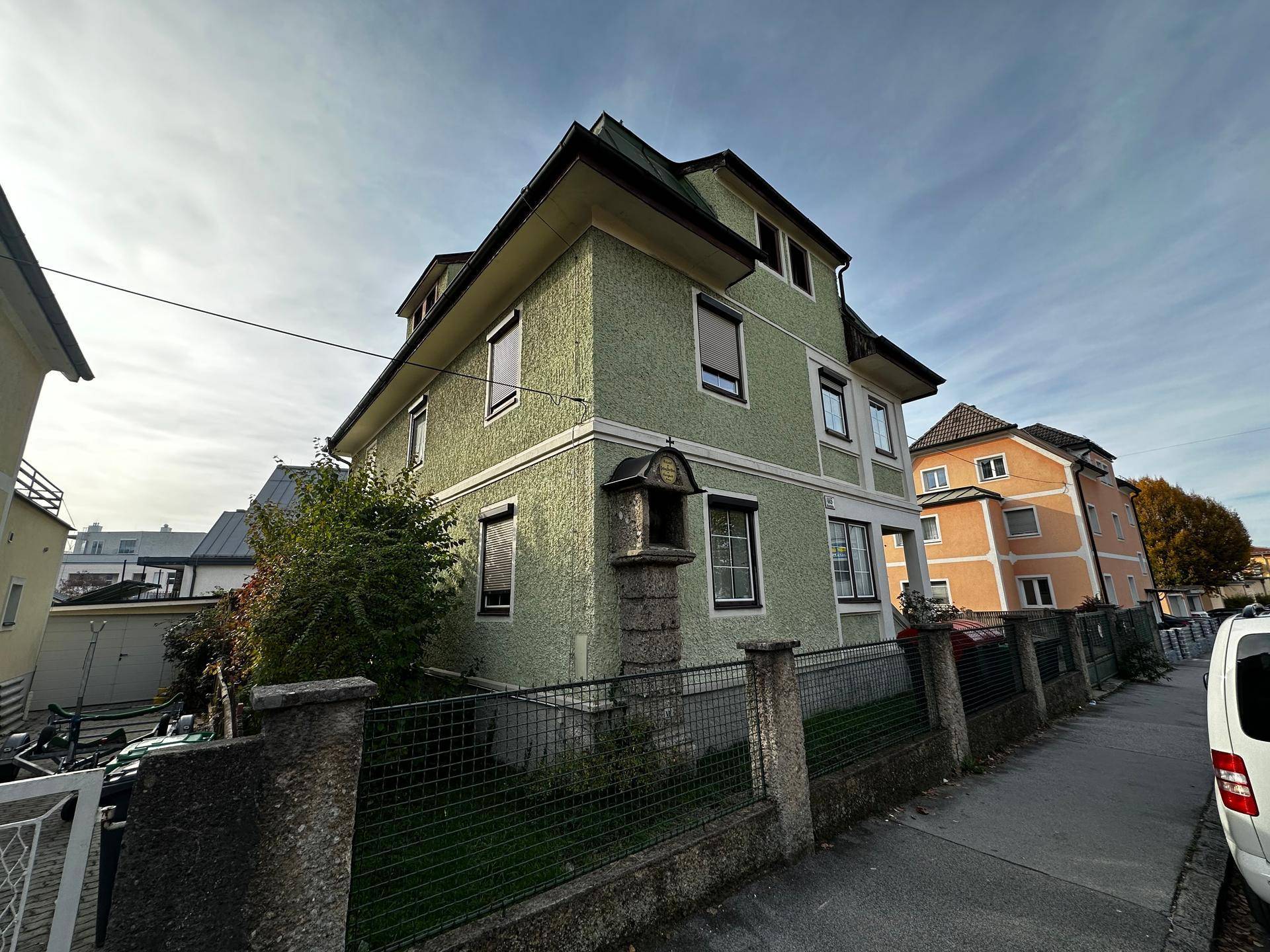 Grünes Wohnhaus mit traditioneller Architektur und kleinem Vorgarten an einer Wohnstraße gelegen.