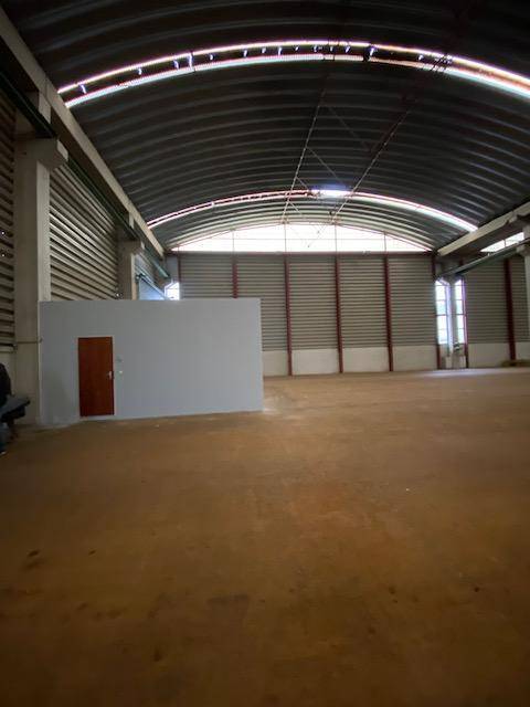Weitläufige Lagerhalle mit einer freistehenden, hellgrauen Box, die eine Holztür und ein Fenster besitzt.