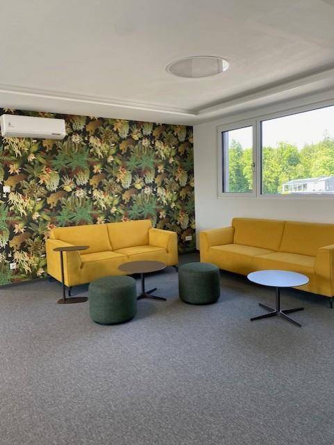 Gemütlicher Loungebereich mit gelben Sofas, grünen Hockern und auffälliger Tapete sowie Klimaanlage.